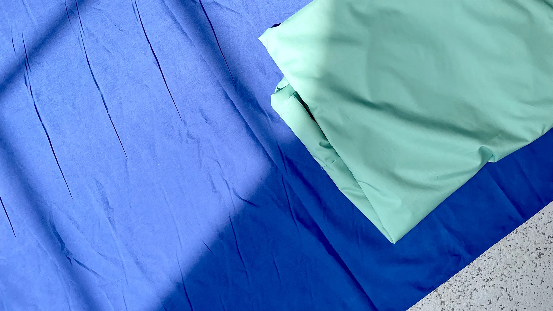 Close up of seagreen and ultramarine fabrics on a concrete floor.