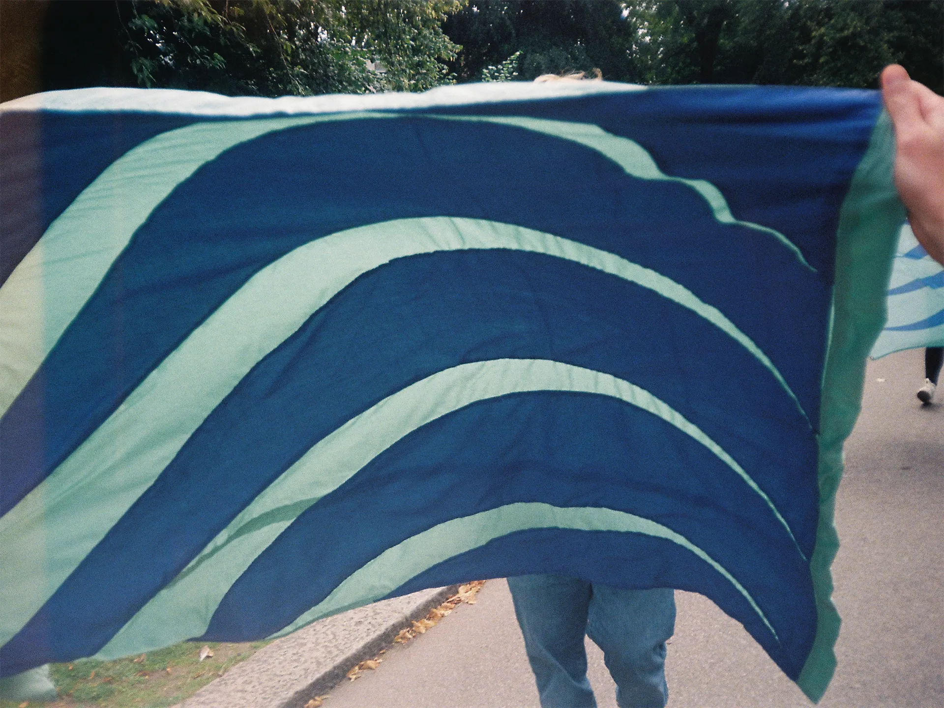 A close up of a person holding a flag. The flag is seagreen and ultramarine blue waves.