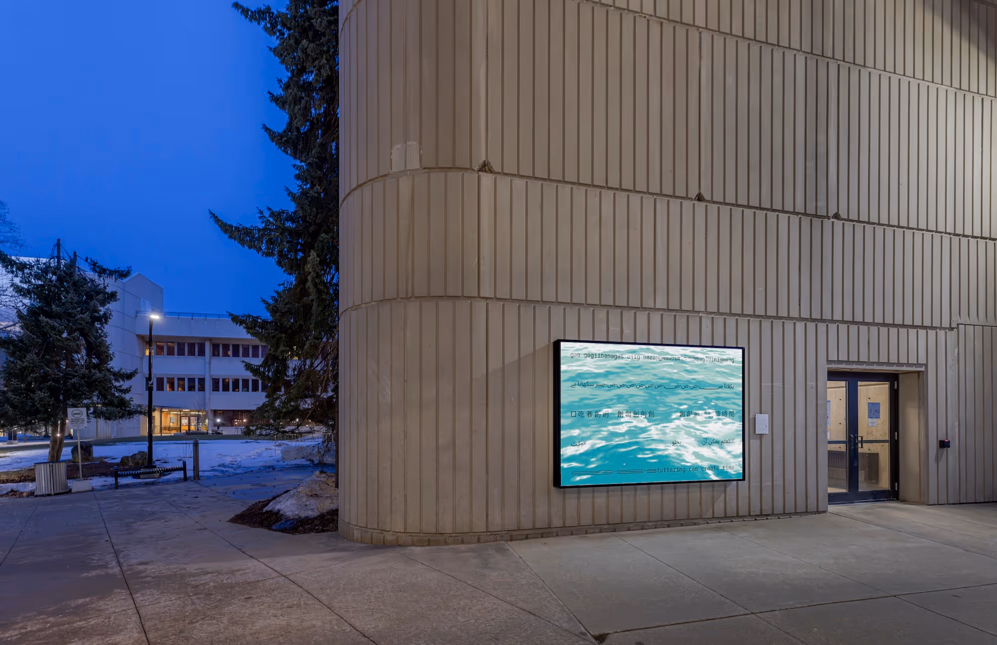 Light shines off the surface of the water. The image is derived from a photograph designer Conor Foran took of Lake Ontario. The text is in a sans-serif typeface organized in five evenly spaced lines, each representing a form of stuttered speech: repeated syllables, repeated words, blocks (pauses in speech), and prolonged syllables. The first line, in Anishinaabemowin, translates to “Stutterers allow/offer a moment.” The word bagidinigeweg ("they allow/offer") is preceded by six overlapping b’s, representing a repetition on the letter b. The second line, in Urdu, translates to “Stuttering teaches patience.” The letter at the beginning of the word صبر ("patience") is stretched and repeats 10 times in a row, representing prolonged sound and repetition. The third line, in Chinese, translates to “People who stutter create time.” The character 創 (the first character of a Chinese word that translates to “create”) appears twelve times in a row, representing repetition. There are intentional spaces after the second and seventh appearance of this character, representing blocks in speech. The fourth line, in Arabic, translates to “Stuttering can create time.” There is an intentional space between التلعثم يمكن أن ("stuttering can") and يخلق ("create"), and an even larger space before الوقت ("time"), representing blocks in speech. The fifth line, in English, reads "Stuttering can create time." The “s” in “stuttering” is stretched horizontally to represent prolonged sound. The Anishinaabemowin and English lines are all lowercase and lack punctuation, giving a casual and informal, almost text message-like feel.