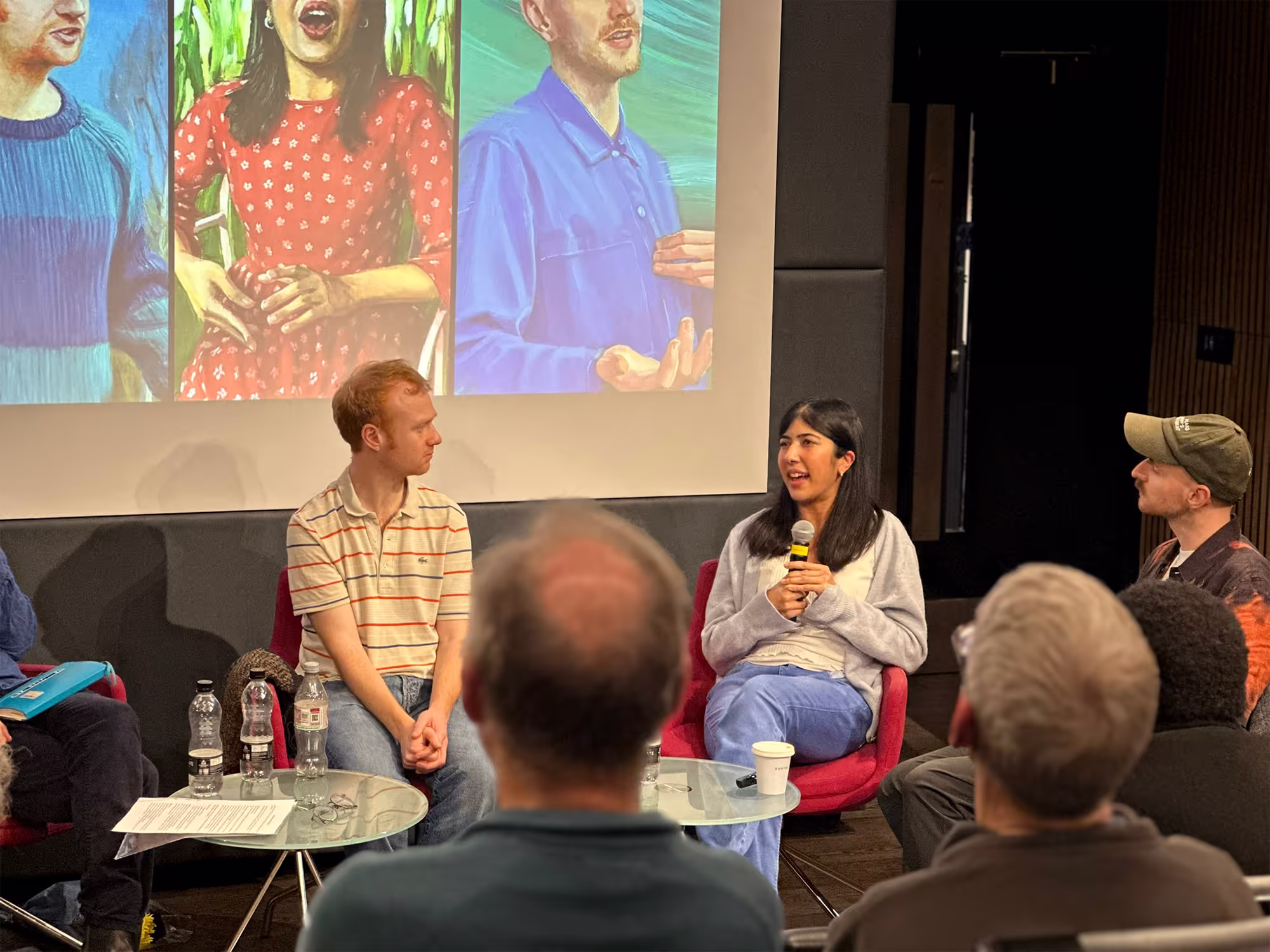 5 people are sat at the top of a seminar room. A crowd is listening to them.
