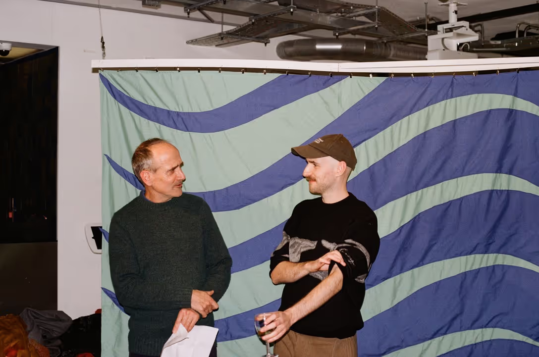 Two men stand in front a blue and green artwork in a gallery.