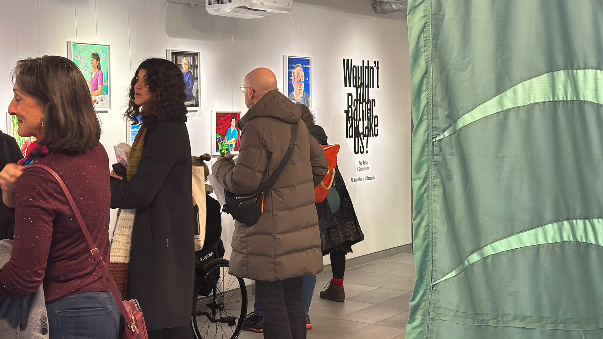 A crowd in an art gallery, looking at artwork and talking.
